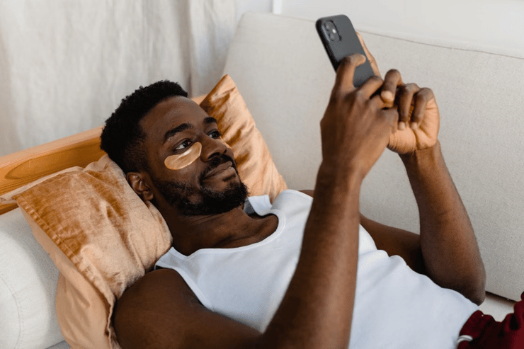 Man using his phone with eyemasks on bed