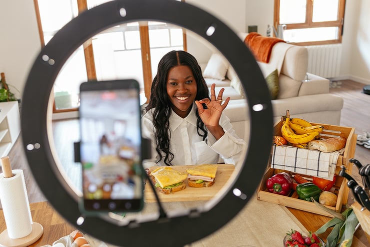 an image showing a woman shooting a video using her phone in front of a ringlight