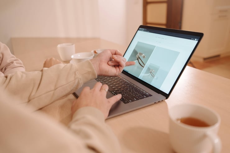 Two individuals working together on a laptop, pointing at the screen with tea cups on the table.